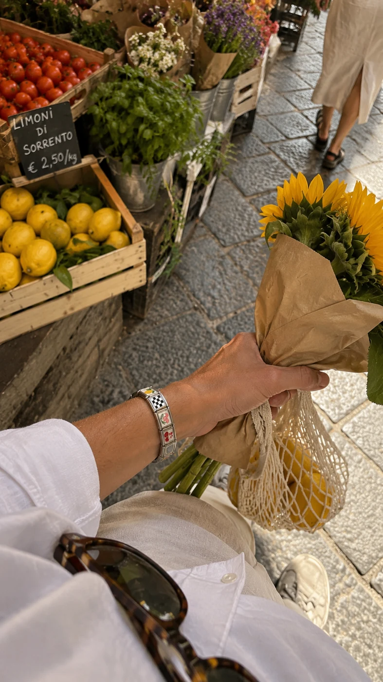 Hand holding sunflowers at a market, wearing a PEZZO bracelet